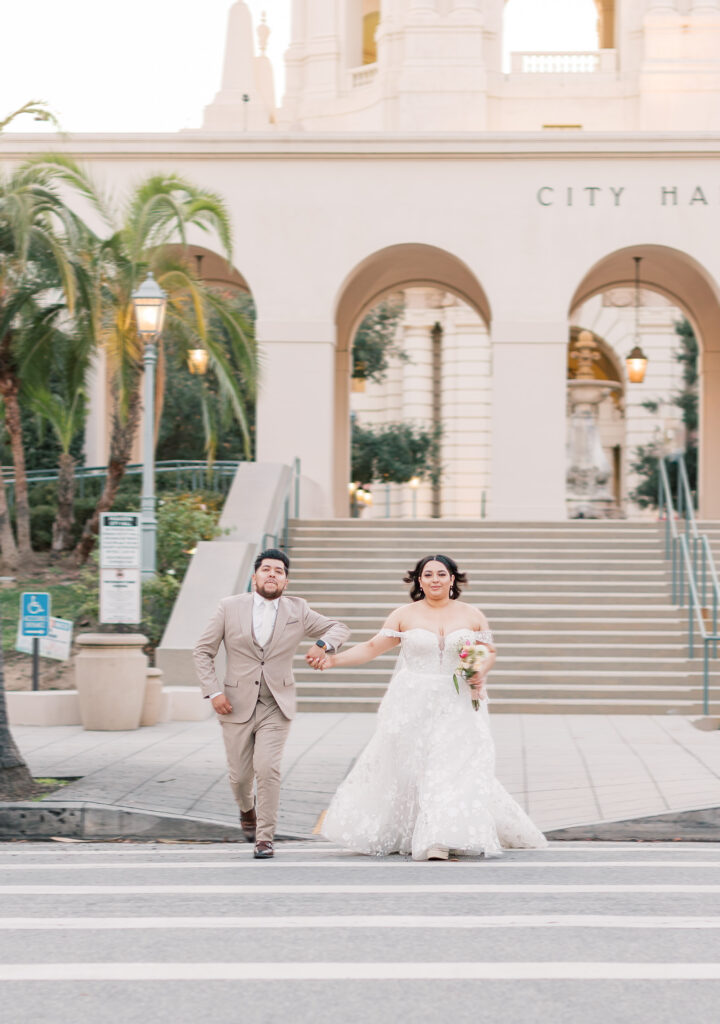 bride and groom are running across a crosswalk at Pasadena City Hall