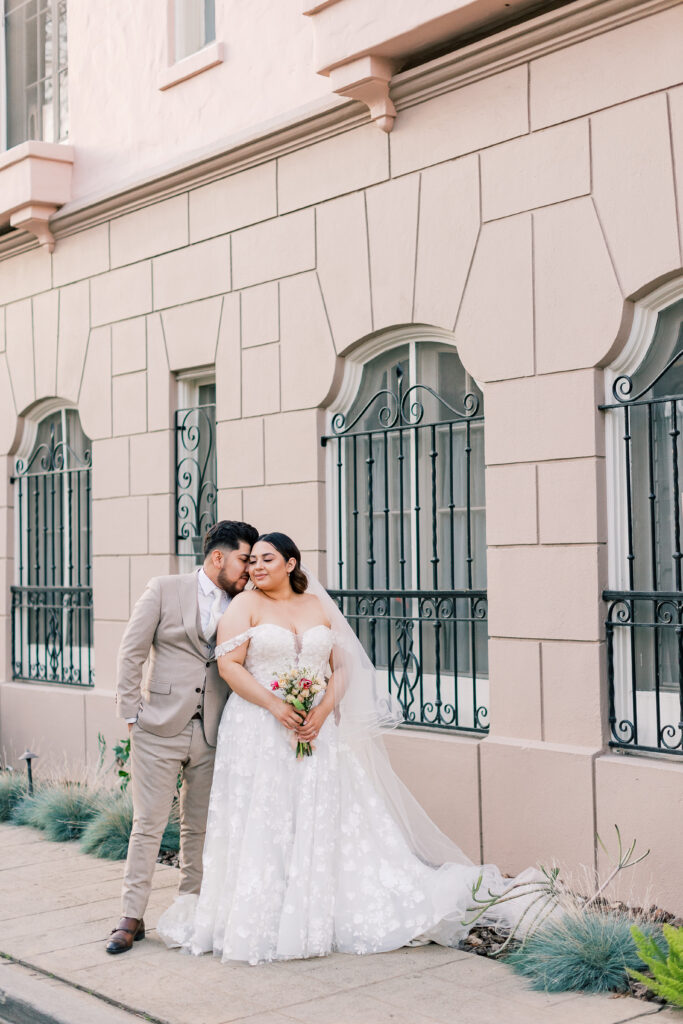 groom nuzzling into his wife in front of a window