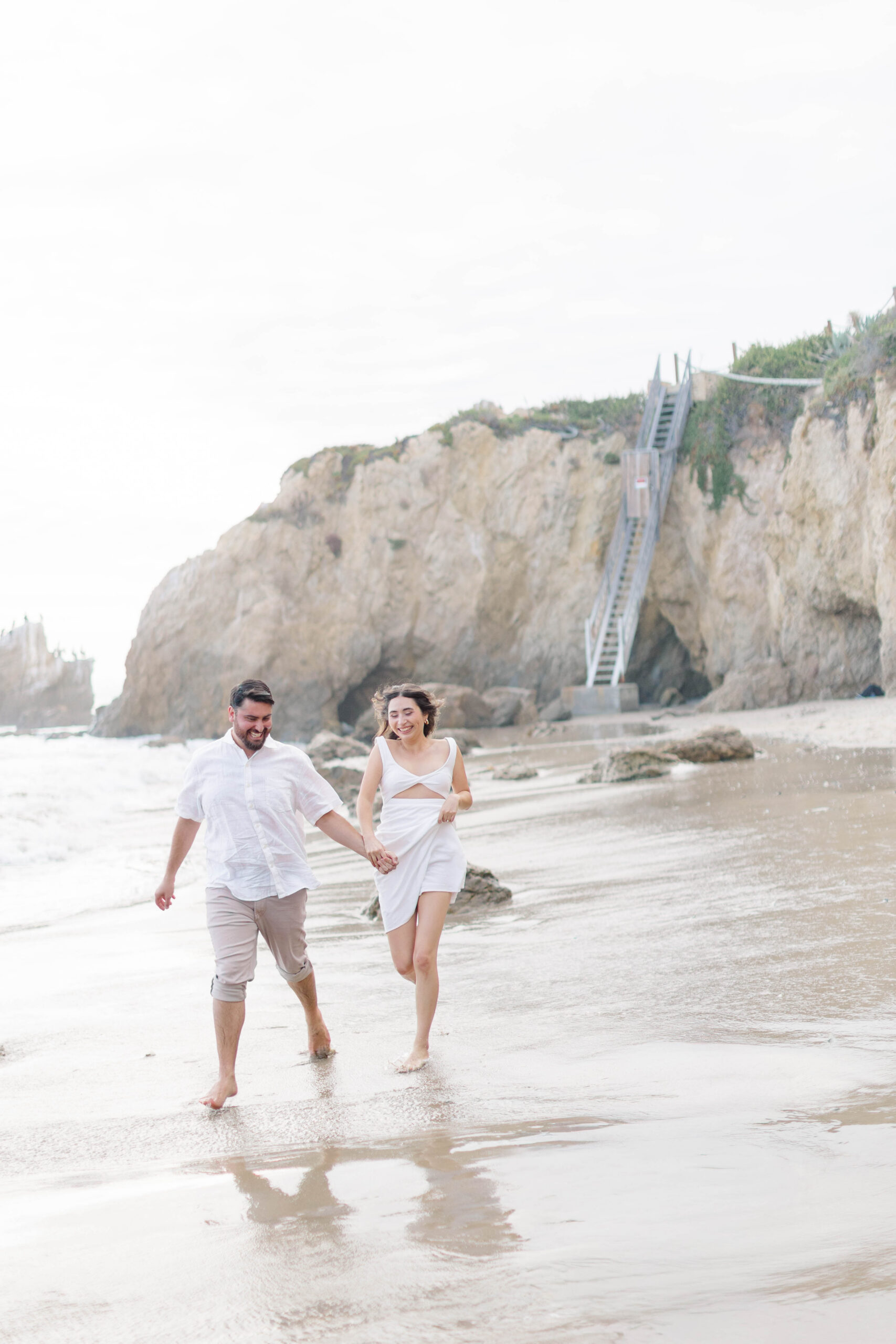 Couple running across the shore at El Matador State Beach, CA